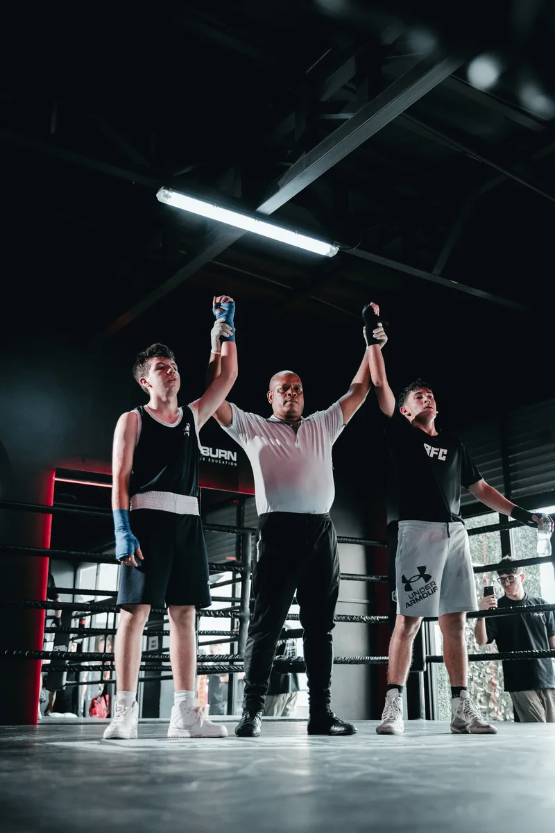 Réferi levanta los brazos de dos boxeadores jóvenes al final de un combate de BFC Warriors